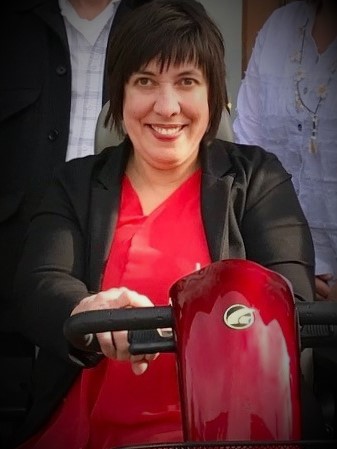 A white woman with short brown hair sits on a red mobility scooter.